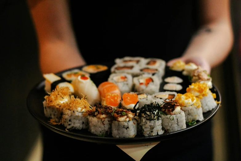 a close up of a person holding a plate of sushi, offering a plate of food