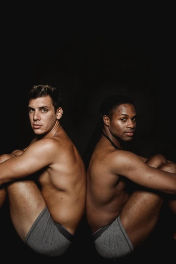 a couple of men sitting next to each other, an album cover, by Jessie Alexandra Dick, unsplash, sporty physique, standing with a black background, olympics, skin color