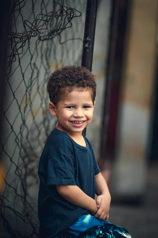 a little boy that is sitting on a skateboard, by Micha Klein, dark short curly hair smiling, portrait of danny gonzalez, standing in an alleyway, color photograph portrait 4k