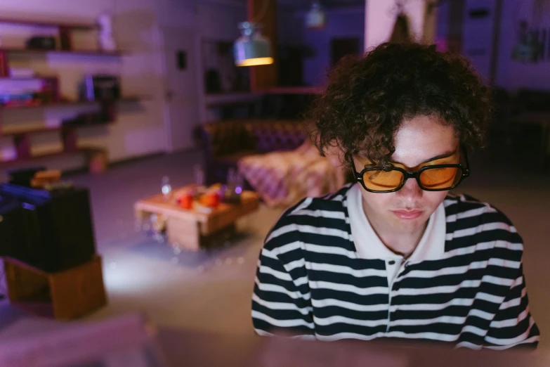 a woman sitting at a table in front of a laptop computer, pexels, video art, wearing 3 d glasses, finn wolfhard, purple and yellow lighting, at home