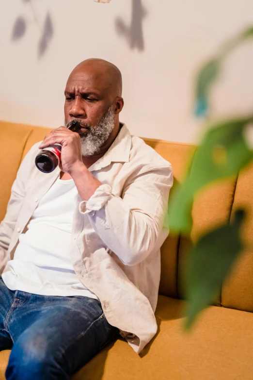 a man sitting on a couch drinking a beer, an album cover, inspired by William Grant Stevenson, pexels contest winner, figuration libre, white beard, black man, ( ( theatrical ) ), holding wine bottle