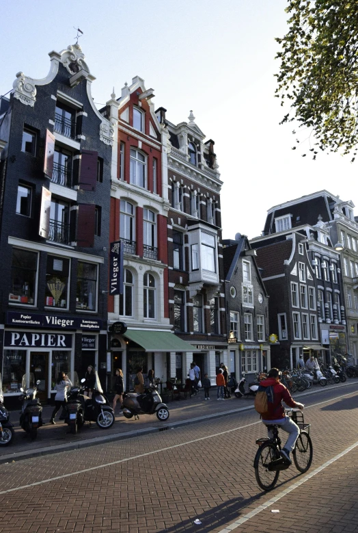 a man riding a bike down a street next to tall buildings, inspired by Cornelis Saftleven, trending on unsplash, art nouveau, view of houses in amsterdam, frank gehry, wikimedia, square