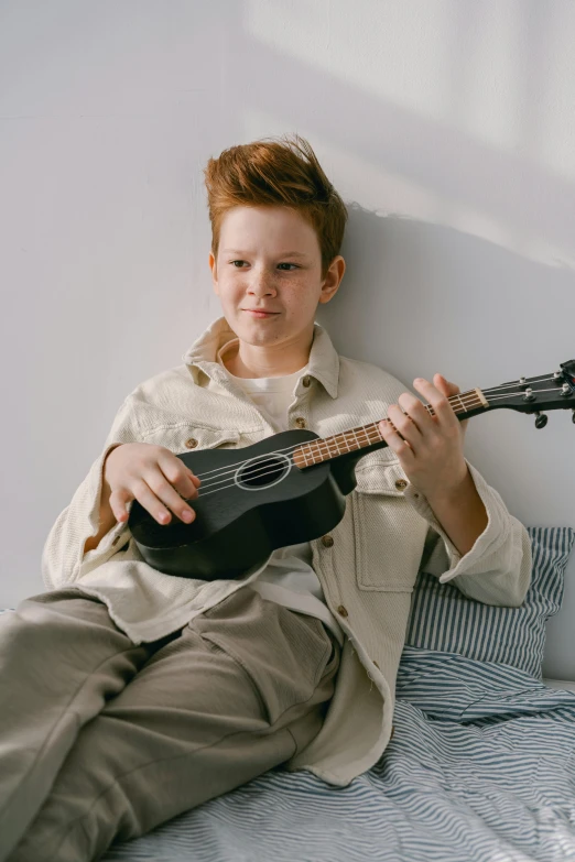 a man sitting on top of a bed holding a guitar, boy with neutral face, on a gray background, promo image, ukulele