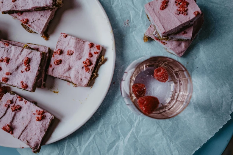 a white plate topped with raspberry brownies next to a glass of water, unsplash, pink concrete, purple, entertaining, thumbnail