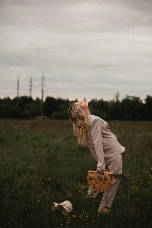 a woman standing on top of a lush green field, pexels contest winner, happening, holding a leather purse, grey sky, dasha taran, captures emotion and movement