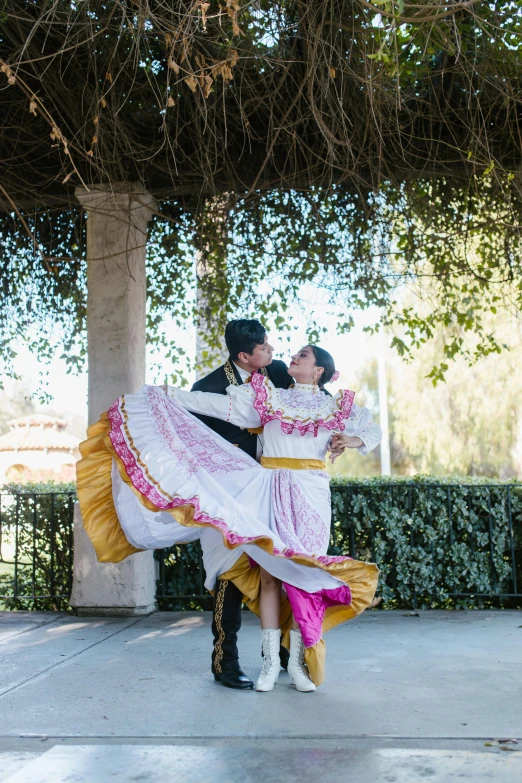 a man and a woman dancing under a tree, she is mexican, white and pink cloth, professional photo, wine