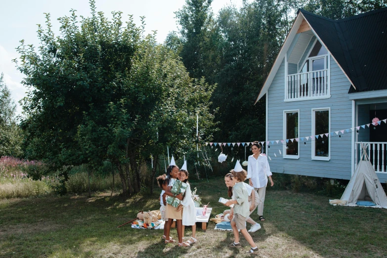 a group of people standing in front of a house, by Julia Pishtar, pexels contest winner, forest picnic, birthday party, white, childish