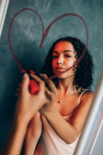 a woman standing in front of a mirror with a heart drawn on it, pexels contest winner, mixed-race woman, holding pencil, chalk, curly