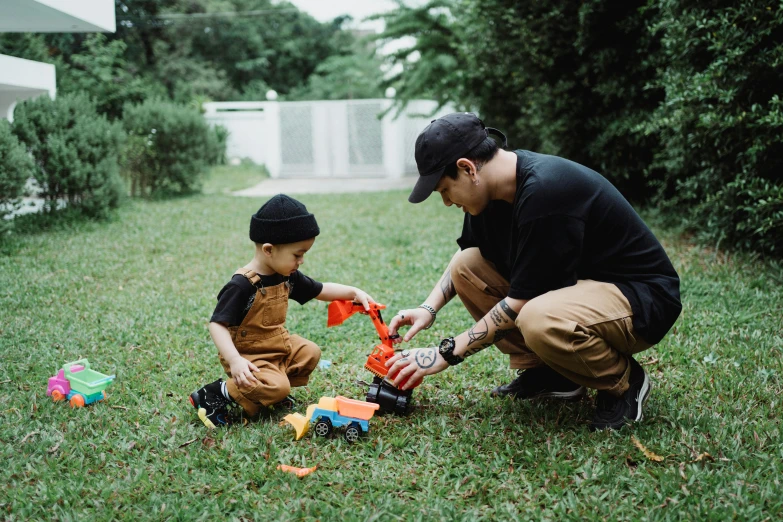a man and a child playing in the grass, by Julia Pishtar, pexels contest winner, kenny wong x pop mart, toys, tattooed, engineer