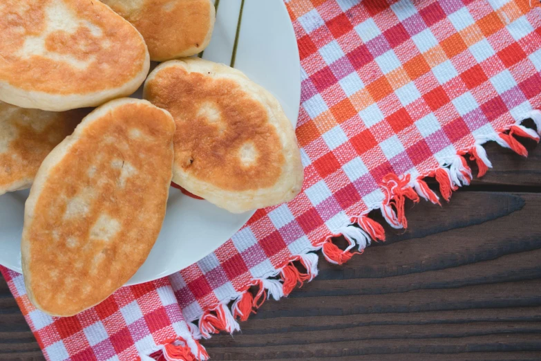 a white plate topped with pancakes on top of a red and white checkered table cloth, inspired by Richmond Barthé, unsplash, dau-al-set, crispy buns, ukrainian, hearts, closeup - view