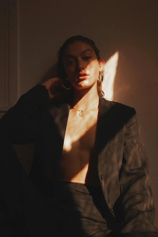 a woman sitting on top of a couch next to a window, an album cover, inspired by Elsa Bleda, trending on pexels, renaissance, wearing a black blazer, sunbathed skin, jewelry, female image in shadow