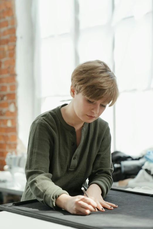 a young man sitting at a table in front of a laptop, inspired by Anna Füssli, wearing a linen shirt, olga zakharova, in a workshop, 2019 trending photo