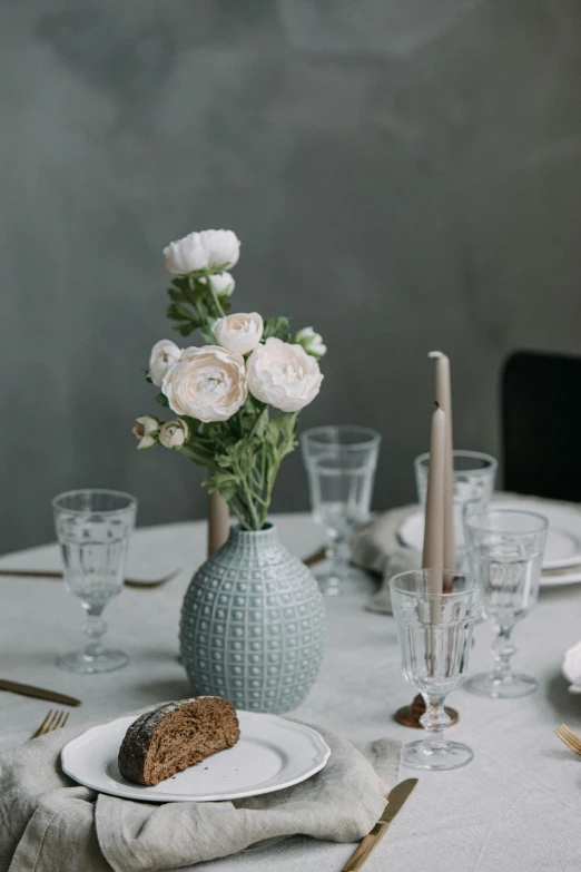 a close up of a plate of food on a table, a still life, inspired by Constantin Hansen, unsplash, vase with flowers, soft grey and blue natural light, tufted softly, long table