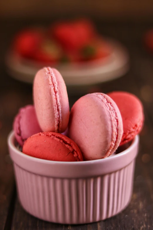 a white bowl filled with pink macarons on top of a wooden table, inspired by Rudolf von Alt, trending on pexels, romanticism, strawberry, red, closeup - view, made of glazed