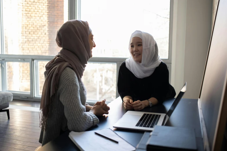 two women sitting at a table with a laptop, hurufiyya, background image, teaching, official screenshot, facing each other