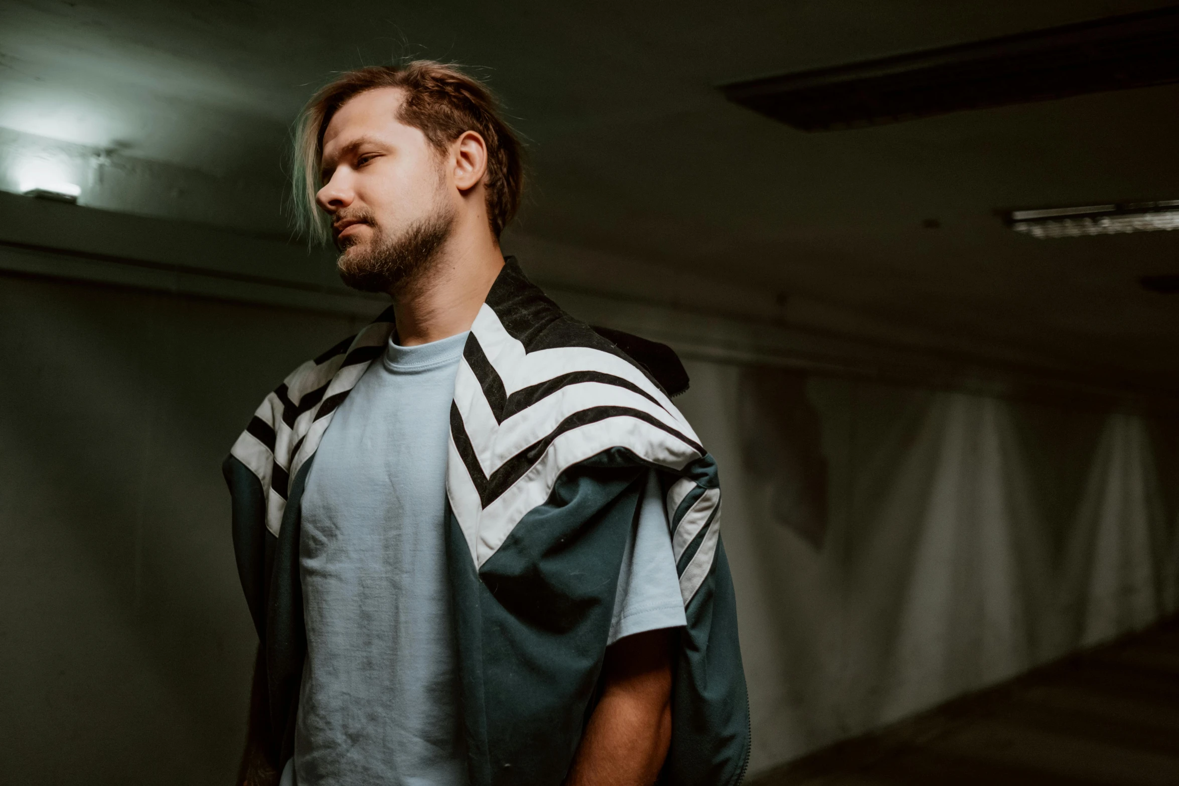 a man is standing in a dark room, an album cover, unsplash, wearing shoulder cape, danila tkachenko, tobey maguire, mrbeast