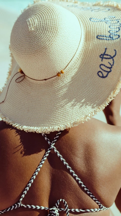 a woman wearing a hat on the beach, by Arabella Rankin, pexels, label, embellishment, navy, back facing