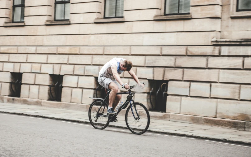 a man riding a bike down a street next to a tall building, pexels contest winner, hammershøi, profile image, student, 1 2 9 7