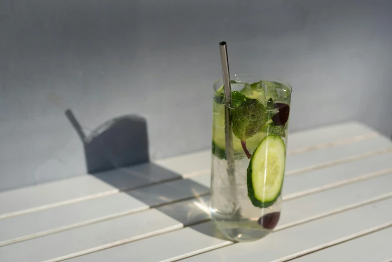 a glass of water with a slice of cucumber in it, unsplash, photorealism, green terrace, glossy white metal, very smoky paris bar, straw