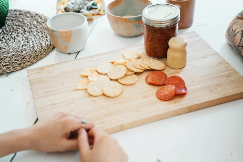 a person cutting up some food on a cutting board, by Jessie Algie, pexels contest winner, process art, jar on a shelf, cheese and pepperoni, on a white table, snacks