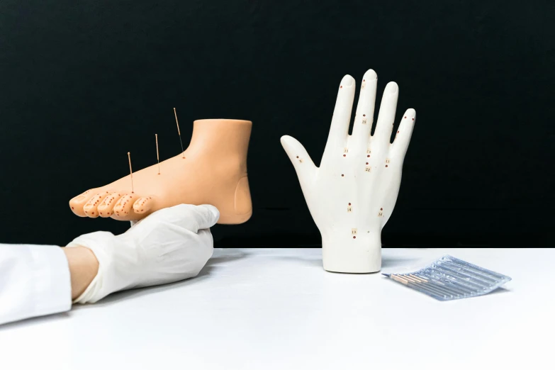 a close up of a person's foot on a table, replicas, needles, a hand, set against a white background