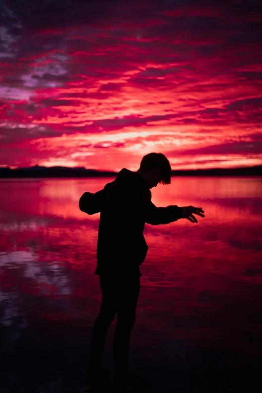 a man standing next to a body of water at sunset, red monochrome, dabbing, aged 13, red cloud light