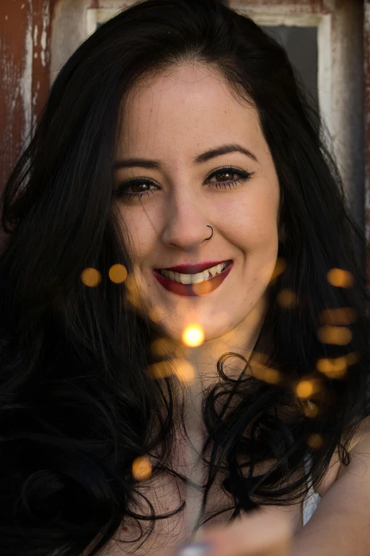 a woman holding a sparkler in front of her face, an album cover, inspired by Lucia Peka, kat dennings, bokeh. chrome accents, smiling woman, ((portrait))