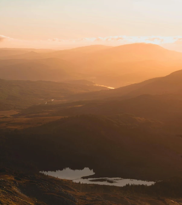 a man standing on top of a mountain next to a lake, by Johannes Voss, unsplash contest winner, hurufiyya, dappled golden sunset, forest plains of north yorkshire, view from high, soft golden light