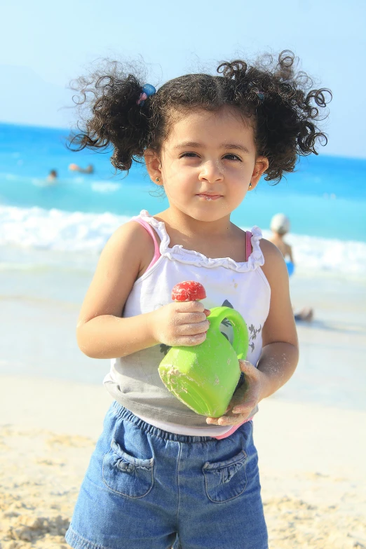 a little girl standing on top of a sandy beach, holding a bottle of arak, fruit, headshot, ameera al-taweel