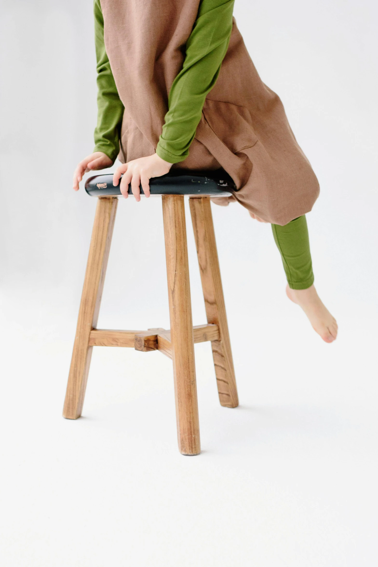 a little girl sitting on top of a wooden stool, unsplash, mingei, detailed product image, wearing pants, oak, 3/4 view