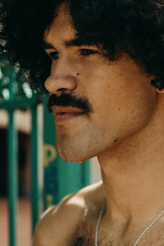 a man with a mustache standing in front of a fence, trending on pexels, long afro hair, mid-shot of a hunky, latino features, neck zoomed in