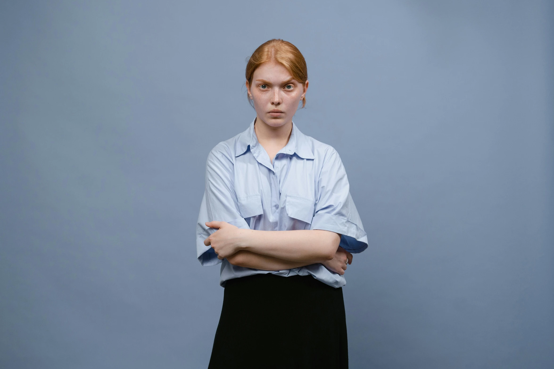 a woman in a blue shirt and black skirt, inspired by August Sander, trending on reddit, hr ginger, angry looking at camera, full frame image, pale blue