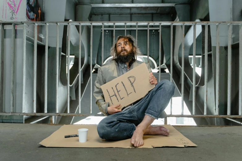 a man sitting on the ground holding a sign, pexels contest winner, renaissance, a photo of a disheveled man, temporary emergency shelter, hungover, prison