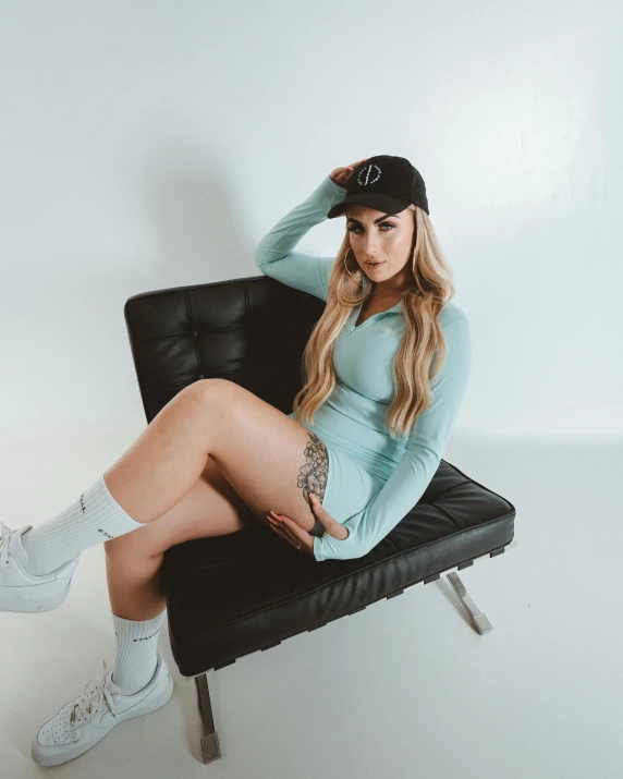 a woman sitting on top of a black chair, by Robbie Trevino, baseball cap, pale blue outfit, official store photo, katelynn mini cute style