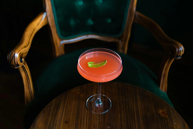 a cocktail sitting on top of a wooden table, by Ndoc Martini, unsplash, renaissance, red velvet furniture, pink and green, flying saucer, seated in royal ease