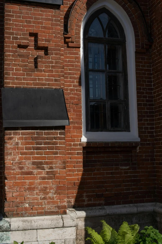 a clock mounted to the side of a brick building, hood and shadows covering face, church window, black house, shot with sony alpha 1 camera