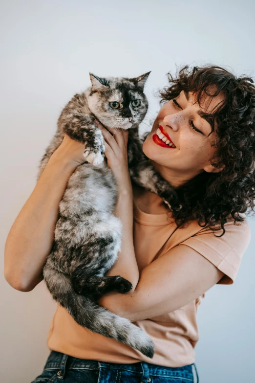 a woman holding a cat in her arms, pexels contest winner, with a curly perm, gray mottled skin, gif, brunette woman