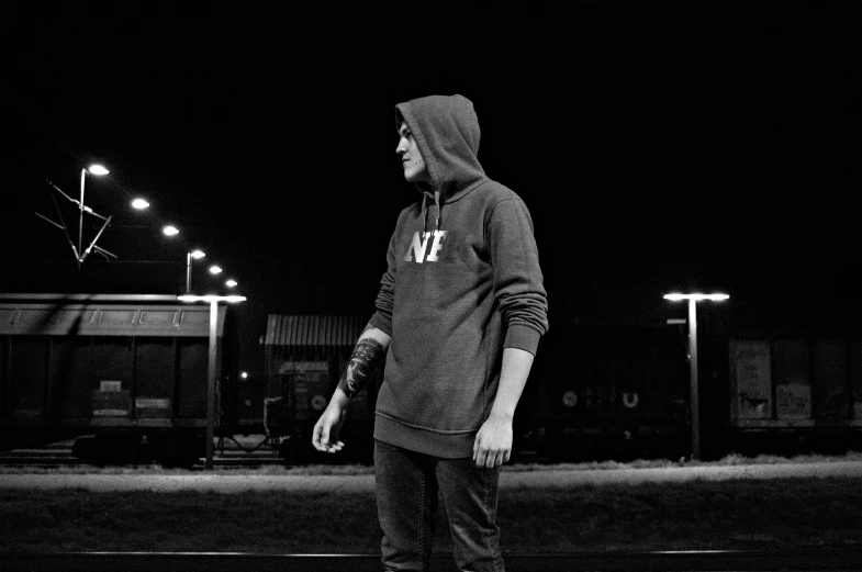 a man riding a skateboard down a street at night, a black and white photo, by Anato Finnstark, unsplash, graffiti, hoodie, standing in a stadium, single portrait, male teenager