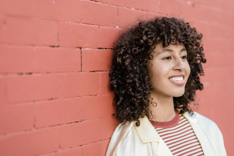 a woman with curly hair leaning against a brick wall, pexels contest winner, on a red background, mixed race, sydney park, ( brown skin )