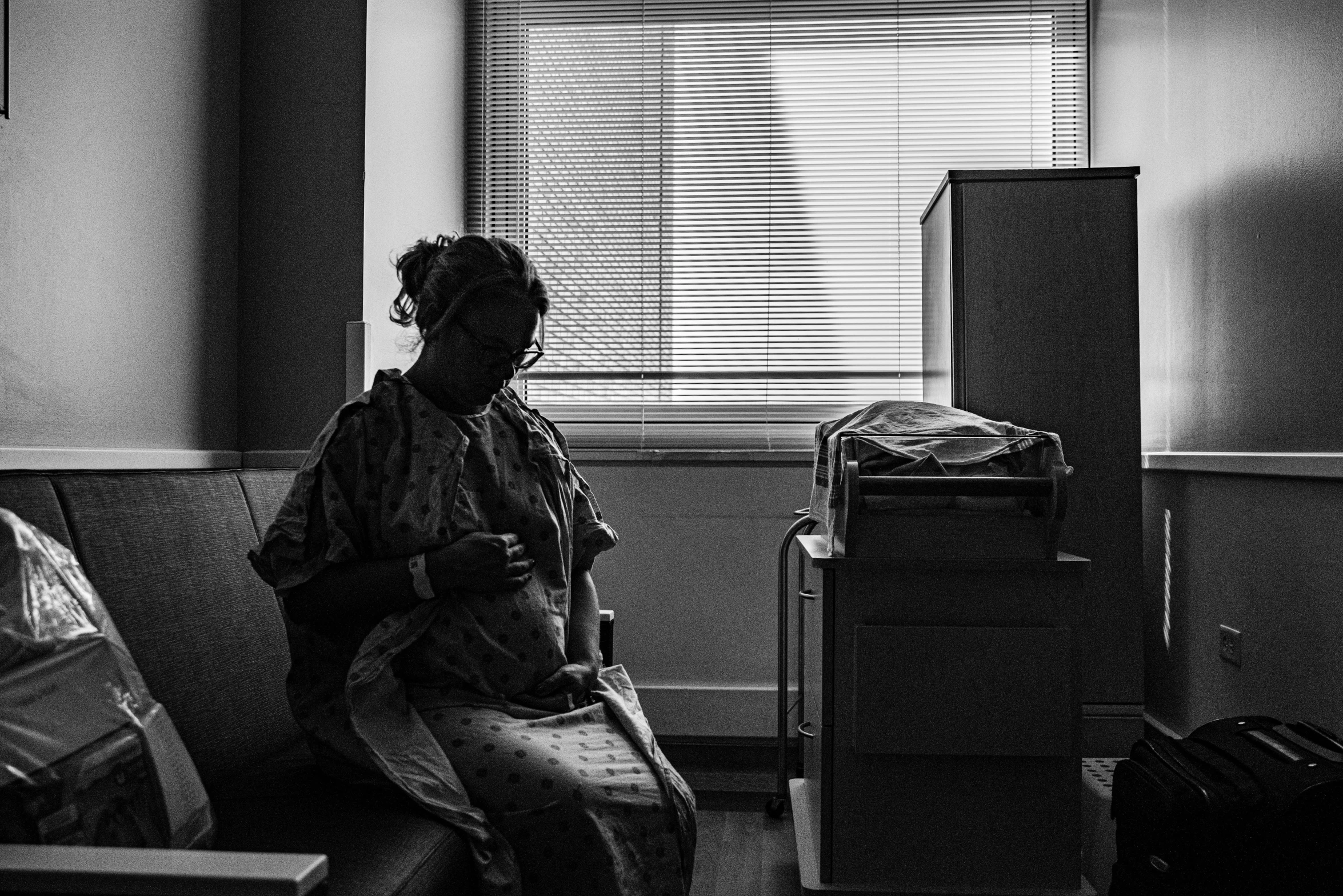 a black and white photo of a woman sitting on a couch, by Dan Frazier, unsplash contest winner, process art, at the hospital in patient gown, pregnant, looking at his phone, photo of a black woman