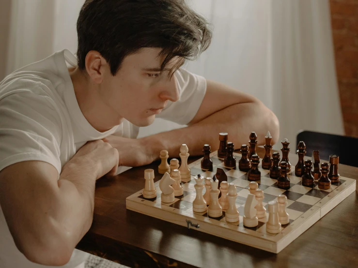a man sitting at a table playing a game of chess, pexels contest winner, profile posing, declan mckenna, looking across the shoulder, looking from shoulder