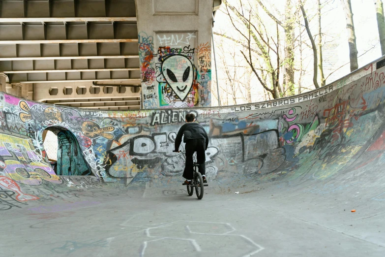 a man riding a bike up the side of a ramp, graffiti, under bridge, creepy themed, berlin park, 2022 photograph