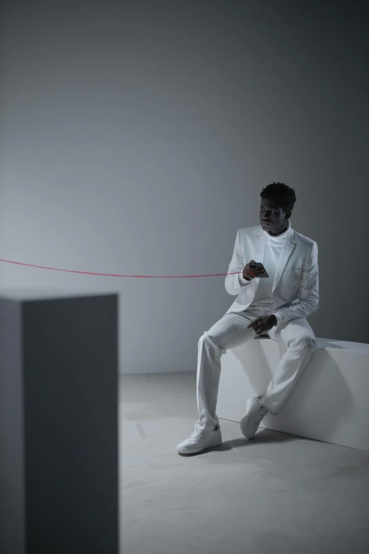 a man in a white suit sitting on a ledge, an album cover, inspired by Carrie Mae Weems, pexels contest winner, bauhaus, wires and strings, adut akech, performing a music video, white room