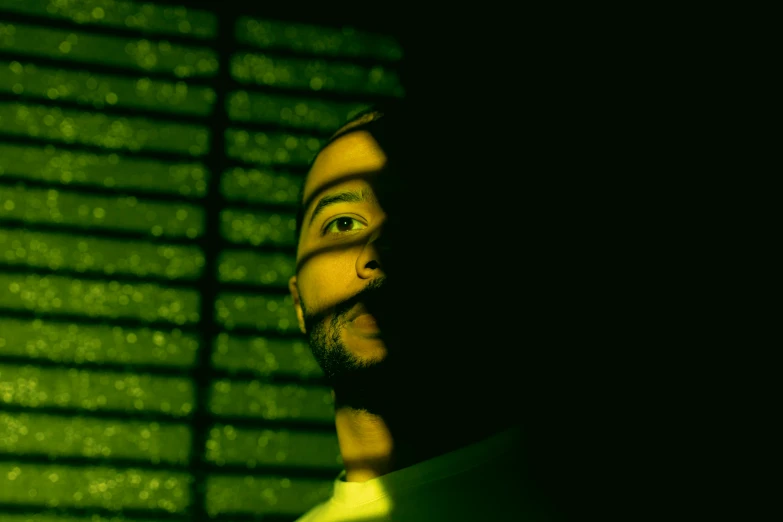 a man standing in front of a green wall, an album cover, inspired by Elsa Bleda, pexels, realism, glowing green neon eyes, difraction from back light, mac miller, consist of shadow