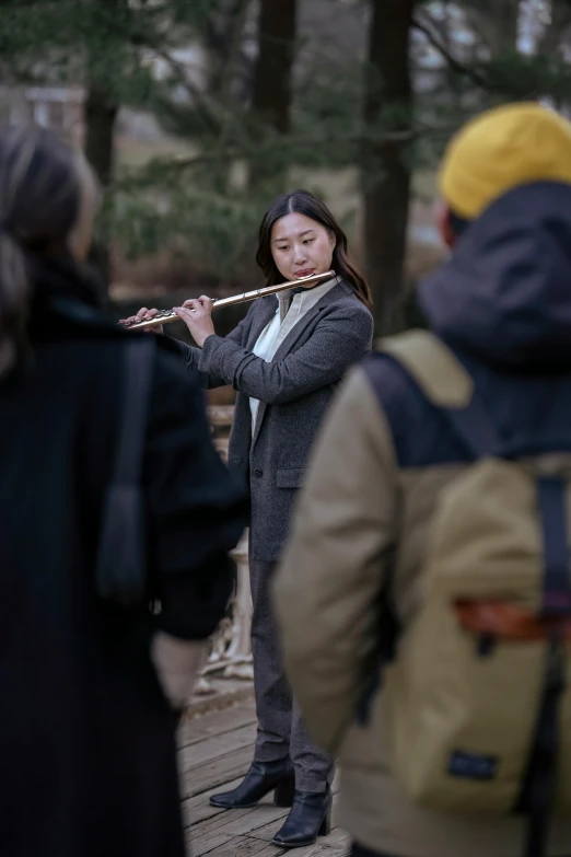 a woman playing a flute in front of a group of people, inspired by Lü Ji, unsplash, sangyeob park, square, b - roll, winter sun