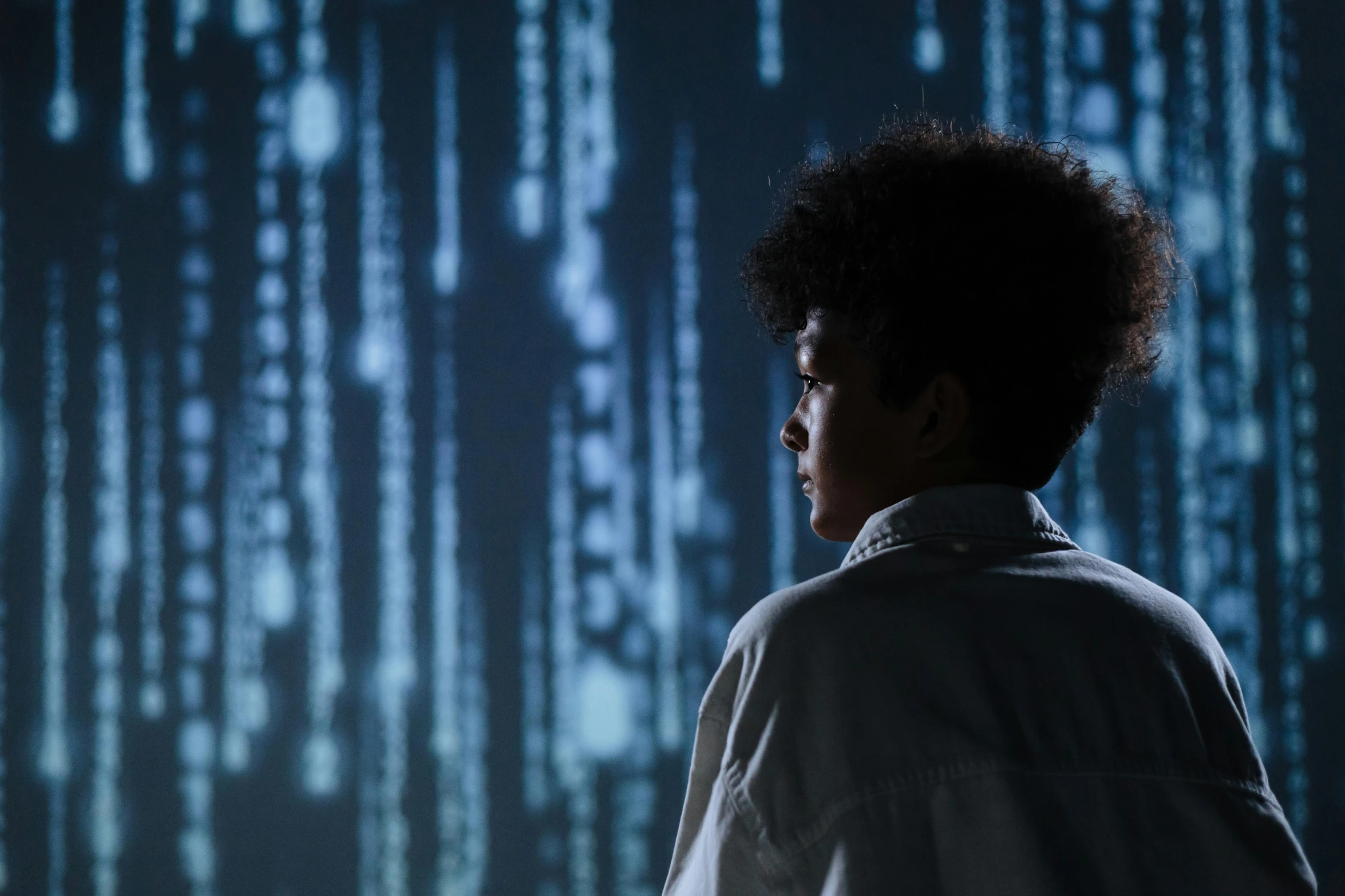 a man standing in front of a computer screen, a hologram, inspired by Ryoji Ikeda, unsplash, afrofuturism, black teenage boy, standing in a server room, portrait of willow smith, tessa thompson inspired