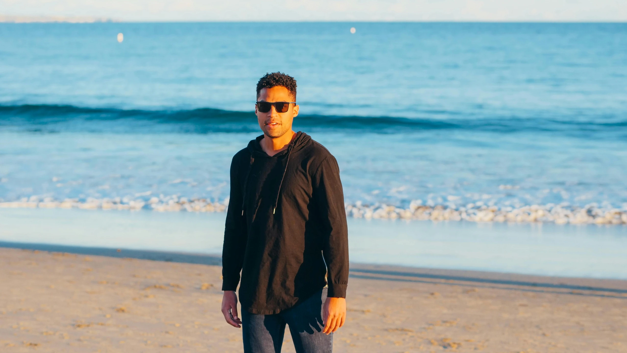 a man riding a skateboard on top of a sandy beach, inspired by Michael Ray Charles, wearing a black hoodie, posing for a picture, oceanside, eric winter