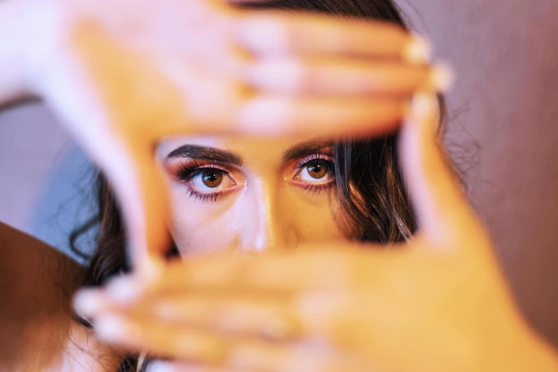 a woman holding her hands in front of her face, trending on pexels, beautiful alison brie magician, eye relections, (colour) eyes, rectangle
