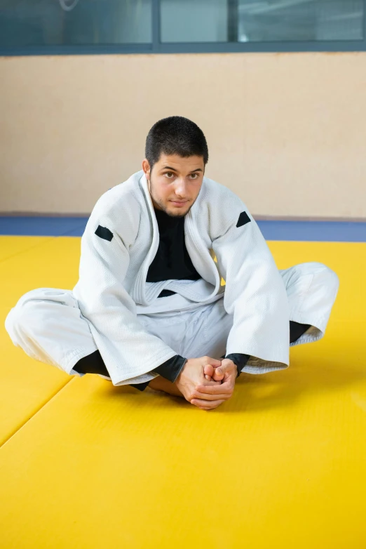 a man sitting on top of a yellow mat, wearing a white gi, sport clothing, professional picture, trending photo