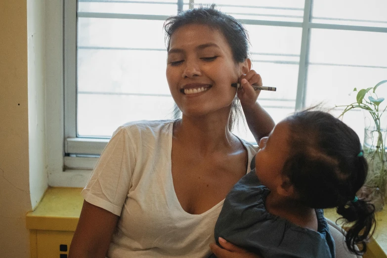 a woman talking on a cell phone while holding a child, with professional makeup, thawan duchanee, beauty mark on cheek, profile image